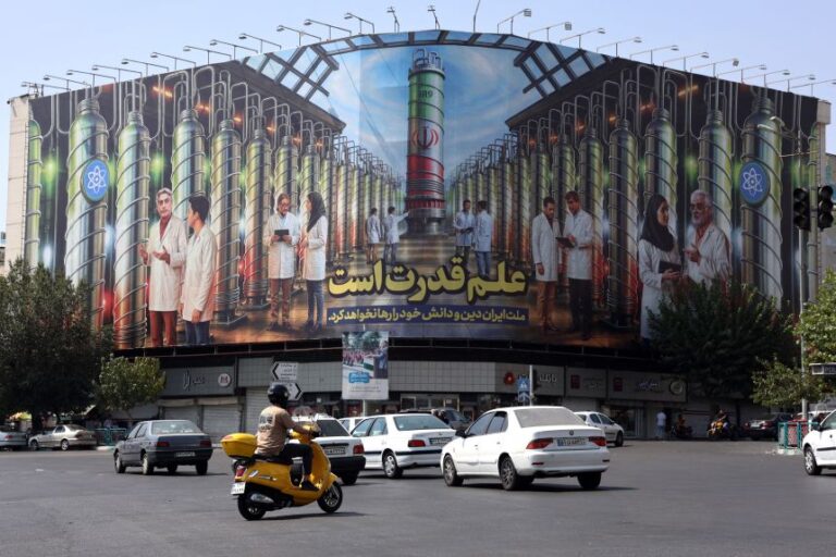 Iranians drive next to a billboard displaying pictures of nuclear scientists, centrifuges and a sentence reading in Farsi: