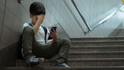 Social issues in internet technology and social media in teenager mental health. Low self esteem young Asian teenager boy sitting alone crying with smartphone, feeling frustration, fear, pain, anxiety, abused as victim of cyberbullying.