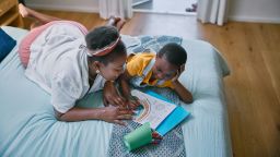 Black woman, child and coloring book on bed with learning, development and support with bonding in home. Mother, boy and paper in bedroom with drawing, art and relax with education in family house