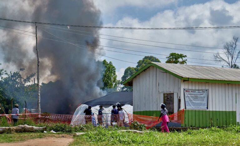 Police and civilians stand near a burning Ebola treatment center in the Democratic Republic of the Congo on May 21, after protesters demanding the return of a victim’s body set fire to the facility.