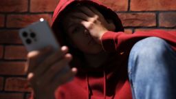 Loneliness concept. Sad teenage boy with smartphone near brick wall, selective focus