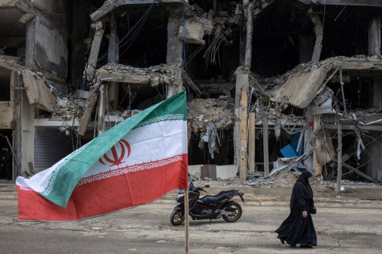 An Iranian flag is seen as a woman walks past damaged buildings amid a ceasefire between Lebanon and Israel, in the southern suburbs of Beirut, Lebanon, on April 20.