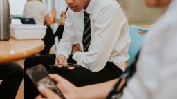 Two school boys stare at their smart phones during the school lunch break in a cafeteria.