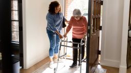 The mid adult woman helps her senior adult friend carefully enter her home.