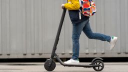 Modern teenager with backpack rides on electric scooter. Boy comes back from school