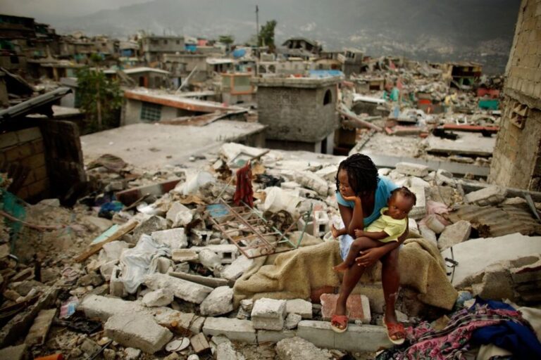 Sherider Anilus, 28, and her daughter, 9-month-old Monica, sit on the spot where her home collapsed during the previous month's 7.0 earthquake in the Fort National neighborhood February 26, 2010 in Port-au-Prince, Haiti. Living in a shack with her husband and two children, Anilus returned to Fort National from a tent camp in downtown Port-au-Prince so to escape the flash flooding that happens when it rains.