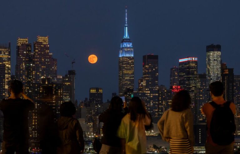 Sky-gazers in Weehawken, New Jersey, photograph the full strawberry moon behind the New York City skyline on June 10, 2025.