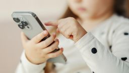 Young child holding a mobile phone, swiping screen, representing screen time and internet usage for digital natives