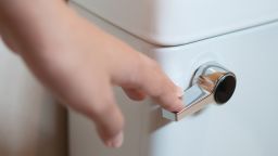 White toilet bowl in a bathroom. Close up of hand holding on Flush valve for clean.