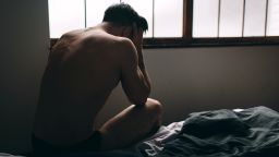 Depressed man sitting on bed in an empty room. This is major depressive disorder.
