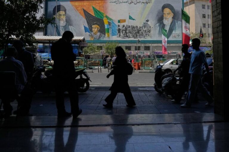 People walk on a sidewalk in front of a mural in Tehran, Iran, on June 8.