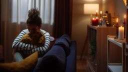 Sad woman sitting on sofa hugging a pillow during the christmas holidays, feeling lonely and depressed