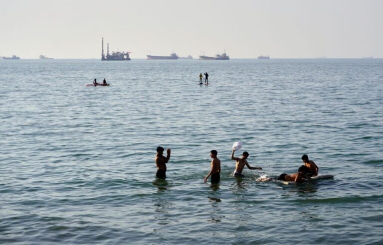 Residents swim and play in the waters of the Strait of Hormuz while cargo ships and commercial vessels lie anchored in the distance off Bandar Abbas, Iran, on Wednesday, June 10.