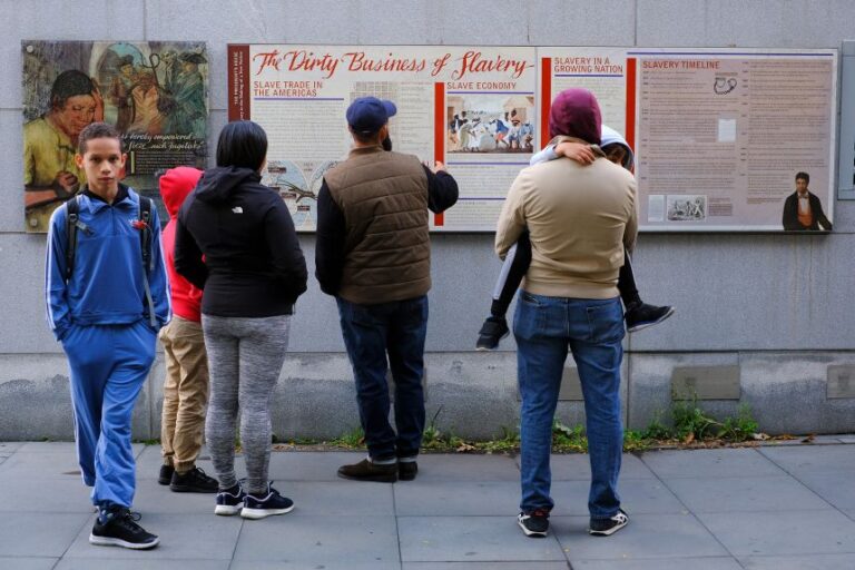 A family reads the signage about slavery on an outdoor exhibit at Independence National Historical Park in Philadelphia, Pennsylvania, on October 24, 2025.
