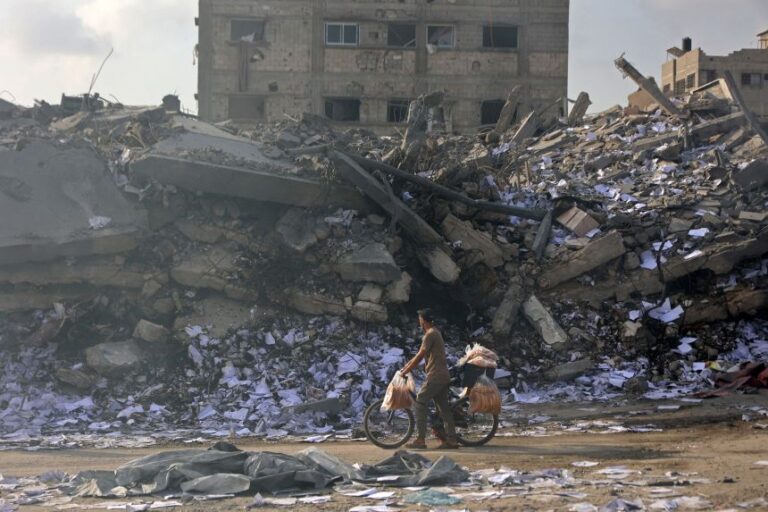A Palestinian vendor pushes his bicycle past the destroyed buildings at the Al-Jalaa street in Gaza City, on July 24, following an Israeli strike.