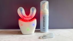The Autobrush Sonic Pro with the red LED lights on, the Autobrush Mint Fluoride Foaming Toothpaste and the tongue scraper attachment against a purple background