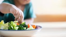 A boy's hand picks up a broccoli in a salad plate.