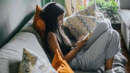 relaxed female hispanic teenager texting on mobile phone. She is sitting on sofa, in sport clothes and is concentrated in the video call