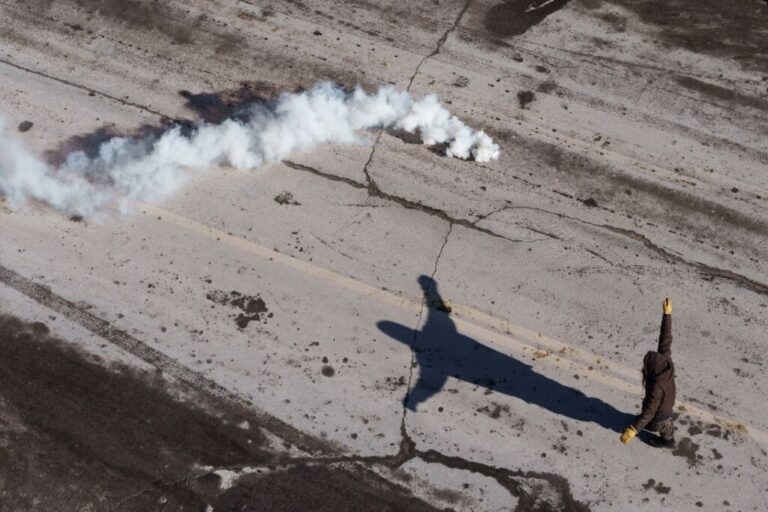 Teargas drifts through the air as a demonstrator holds up his arms and shouts at federal agents, near the site where Alex Pretti was fatally shot by federal agents, on January 24.
