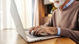 Close up of older trendy executive sitting at home and working remotely on a laptop.