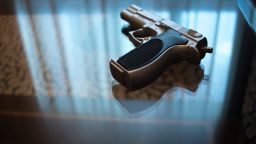 Automatic pistol gun on glass table in bedroom in luxury hotel in silhouette with reflection of window light.