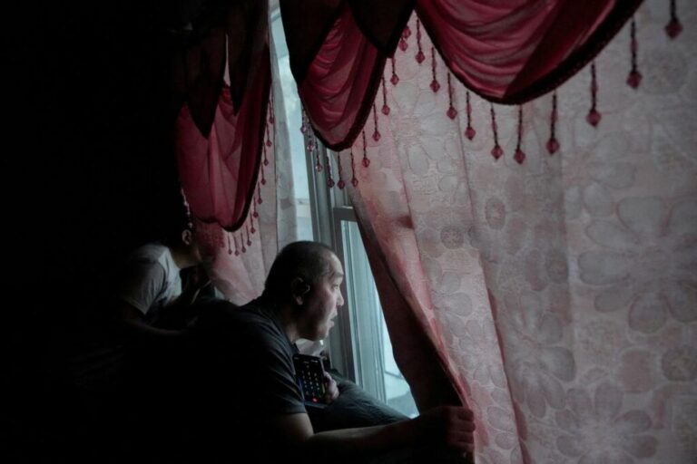 Thao looks out the window with his son Chris as several vehicles with ICE agents idle in the street outside of their home a day after he was taken from his home.