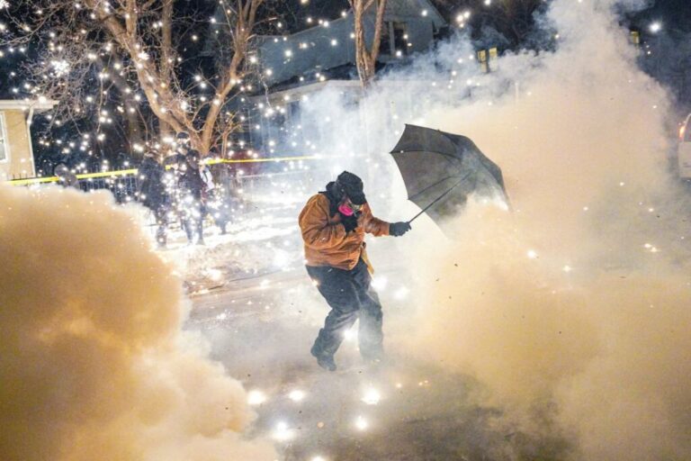 A protester attempts to protect themselves as federal agents fire munitions and pepper balls, in north Minneapolis, on January 14.
