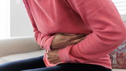 Close-up of unrecognizable black woman sitting on couch holding her abdomen in pain