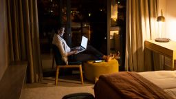 Wide shot of African female using laptop in hotel room at night
