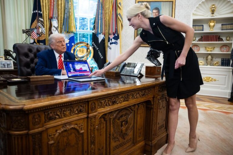 President Donald Trump looks on as Natalie Harp, an aide, places a computer playing a news report about the stock market during a press conference in the Oval Office at the White House May 30, 2025.