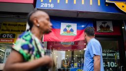 People walk past a restaurant displaying Haitian flags in the Little Haiti neighborhood of Brooklyn, New York, on July 29, 2026.