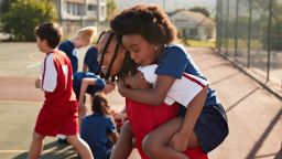 Playful girl piggybacking friend during sports day in schoolyard