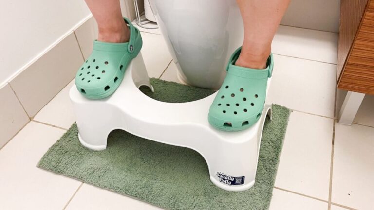 Person with teal Crocs using a white toilet stool