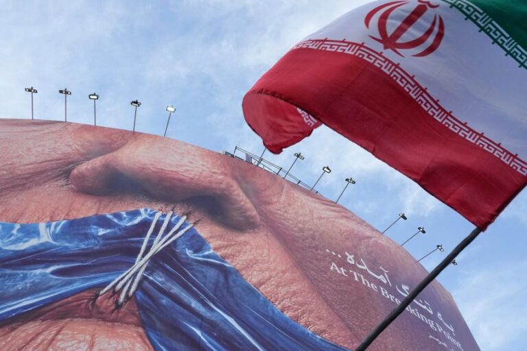 An Iranian flag is waved under a billboard with graphic showing Strait of Hormuz and the sewn lips of President Donald Trump, in downtown Tehran, Iran, on May 6.