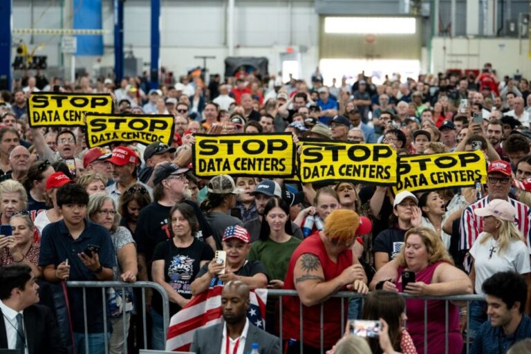 Demonstrators hold up anti-data center signs as President Donald Trump speaks at a General Motors facility in Milford, Michigan, in July.