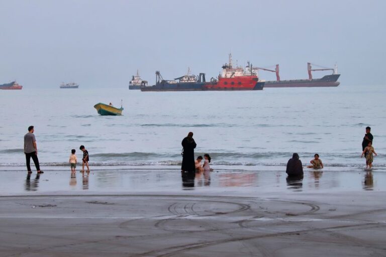 People spend time at a beach as commercial vessels are anchored in the Strait of Hormuz off Bandar Abbas, Iran, on August 5.