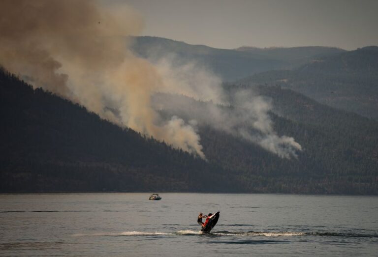 A person rides a personal watercraft on Okanagan Lake, in Lake Country, British Columbia, as the Quilpituk Creek wildfire burns on the mountainside across the lake near Fintry, on August 3.