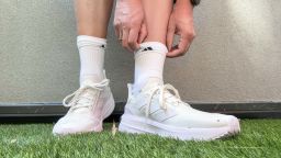 A woman putting on Adidas shoes for heel pain.