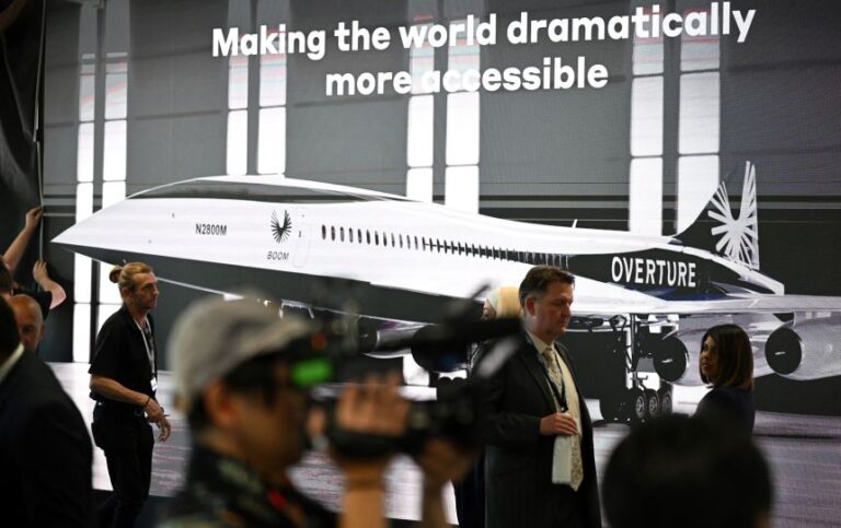 Attendees walk past a poster of Boom Supersonic's Overture aircraft concept at the Farnborough Airshow, in England's county of Hampshire, in July 2022.