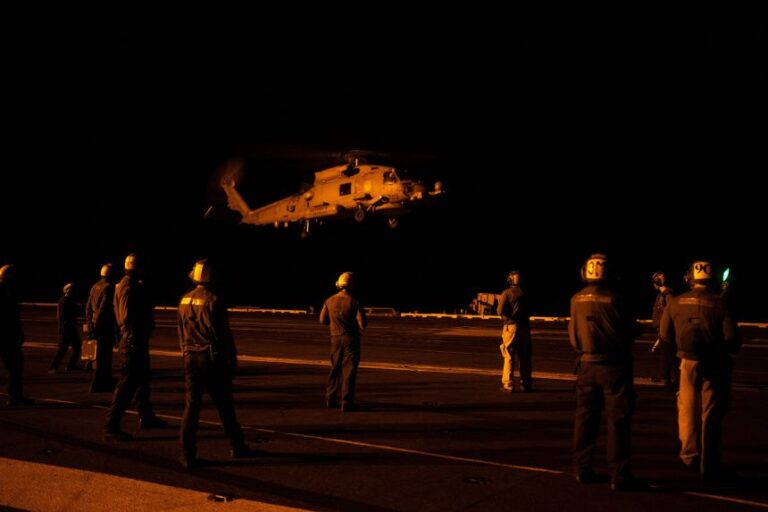 US Navy sailors guide a helicopter as it lands during nighttime operations on the flight deck of the USS George Washington in the Arabian Sea on September 12, 2026.