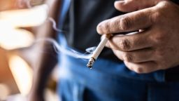 Detail of a man holding a smoking cigarette in his hand.