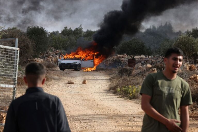 Palestinians stand near a burning car reportedly set alight by Israeli settlers attempting to disrupt them harvesting olives near Turmos in the West Bank in October 2025.