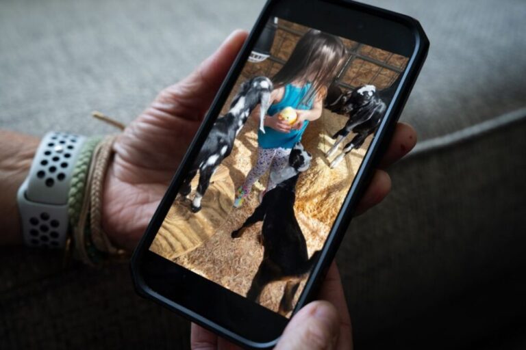 Emily Marris shows an old cell phone photo at her home in Murrieta, California on March 27, 2026. In the image, her daughter Alana Rey Marris, now 5, plays with baby goats on a farm in Temecula, where Emily had purchased raw milk from due to concerns over breastfeeding her youngest daughter, Brooklyn while taking medication. In 2025, Brooklyn was hospitalized and went into cardiac arrest three times after consuming unpasteurized goat milk.