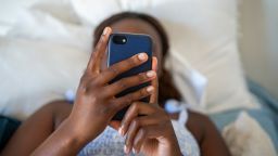 Close-up of a young teenage girl using a smart phone while lying alone on her bed at home