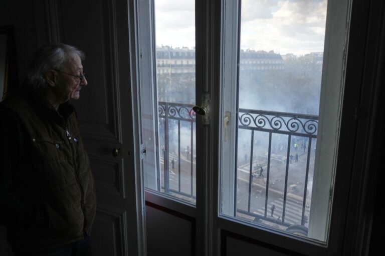 A man watches through his window as protesters clash with police during a demonstration in Paris on Saturday.
